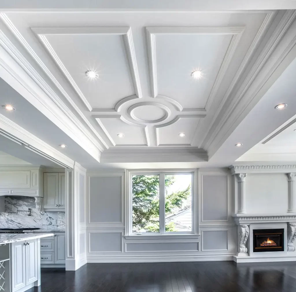 Luxurious white interior featuring an ornate coffered ceiling, decorative wall paneling, marble fireplace, and dark hardwood floors in an elegant open-concept living space.