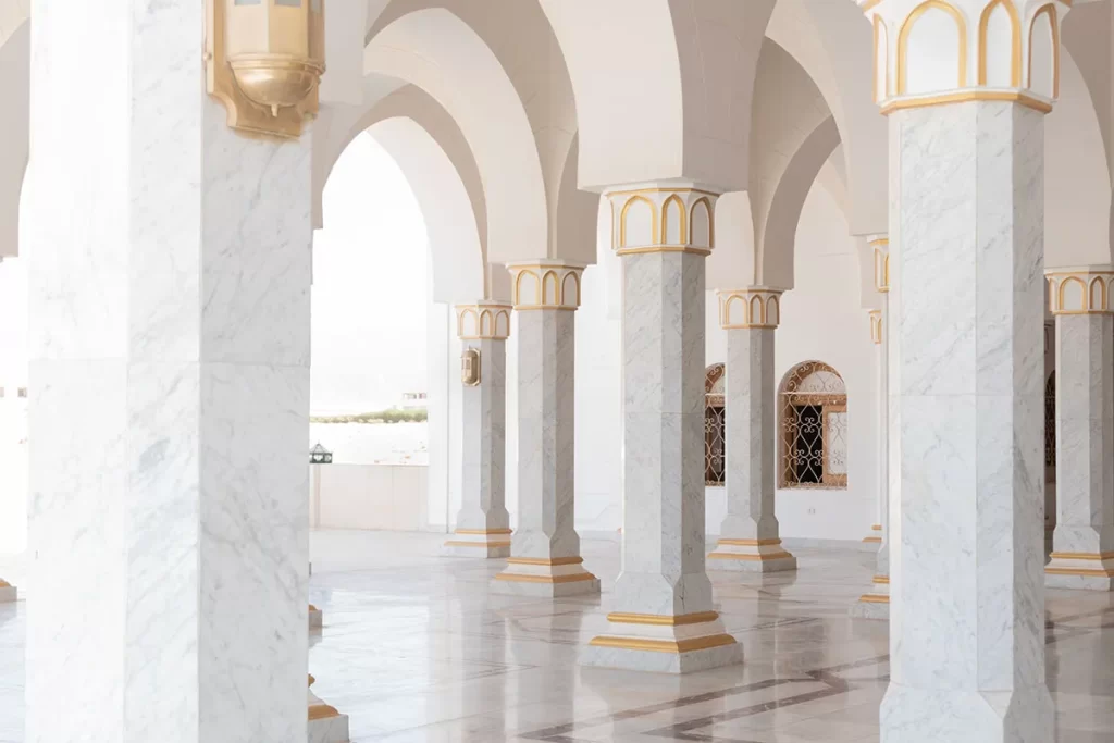Elegant white marble colonnade with gold accents creating a series of arches in what appears to be a mosque or palatial building.