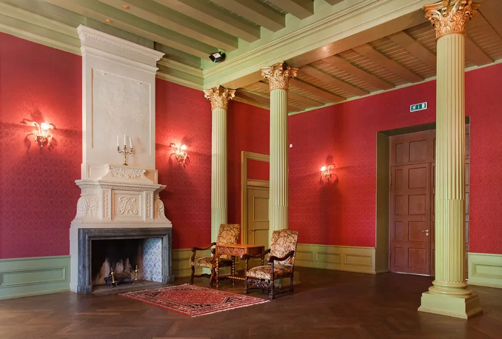 Grand classical room with crimson walls, mint green ceiling, gold fluted columns, ornate fireplace, and period furniture. 
