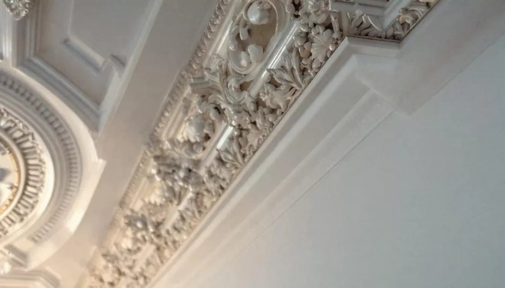 The image features a beautifully crafted room showcasing elegant plaster crown moldings along the ceiling, seamlessly blending with the walls. This design element highlights the durability and timeless style of plaster materials, creating a harmonious and visually appealing space.